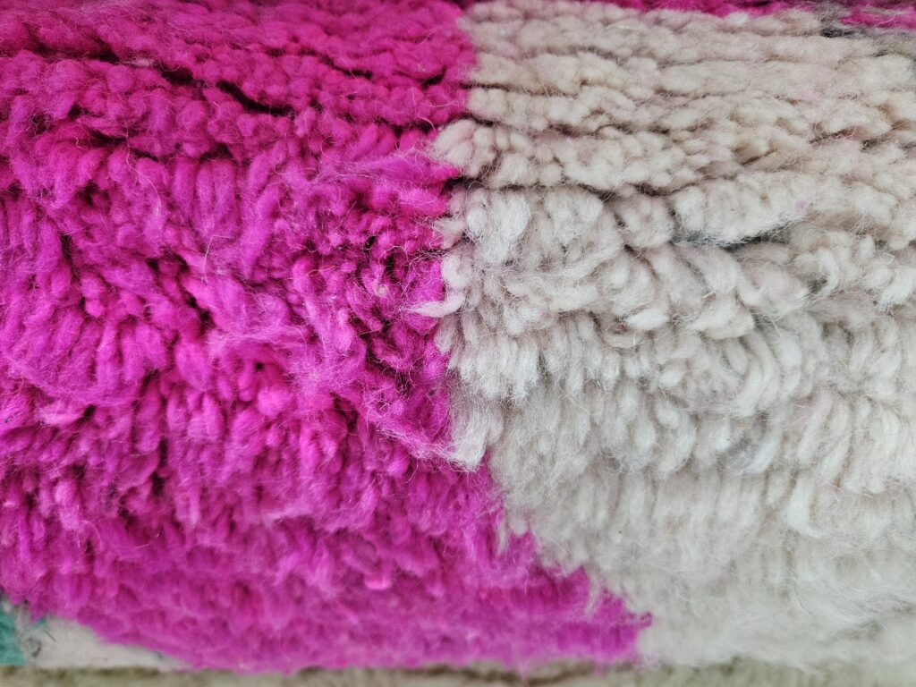 Close-up van een weelderig Berber tapijt met een rijke textuur in opvallend roze en natuurlijk crème wol.