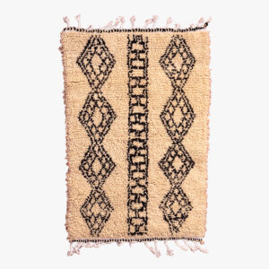 Traditioneel berber tapijt met beige achtergrond en zwarte diamant- en ladderpatronen, afgewerkt met roze franjes.