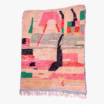 Abstract handgeweven berber tapijt in pastelroze met zwarte, groene, en rode abstracte patronen en franjes.
