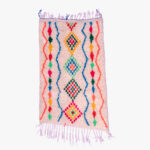 Traditioneel berber tapijt met een dynamisch patroon van geometrische figuren in roze, blauw, groen en geel op een crèmekleurige achtergrond.