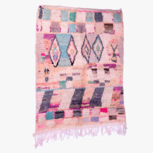 Handgeweven berber tapijt met een veelkleurig patroon van geometrische vormen en abstracte blokken op een zachtroze achtergrond.