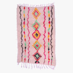Kleurrijk handgeweven berber tapijt met traditionele patronen in roze, zwart, en accenten van groen en geel.
