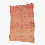 Traditioneel oranje berber tapijt met ingewikkelde witte en gele geometrische patronen en een versierde rand.