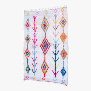 Wit Berber tapijt versierd met kleurrijke, traditionele diamantvormige patronen en botanische designs, perfect voor een hedendaags interieur.