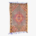 Traditioneel Berber tapijt met centraal diamantmedaillon in rode en oranje tinten, omgeven door een decoratieve aardekleurige rand met bloempatronen.