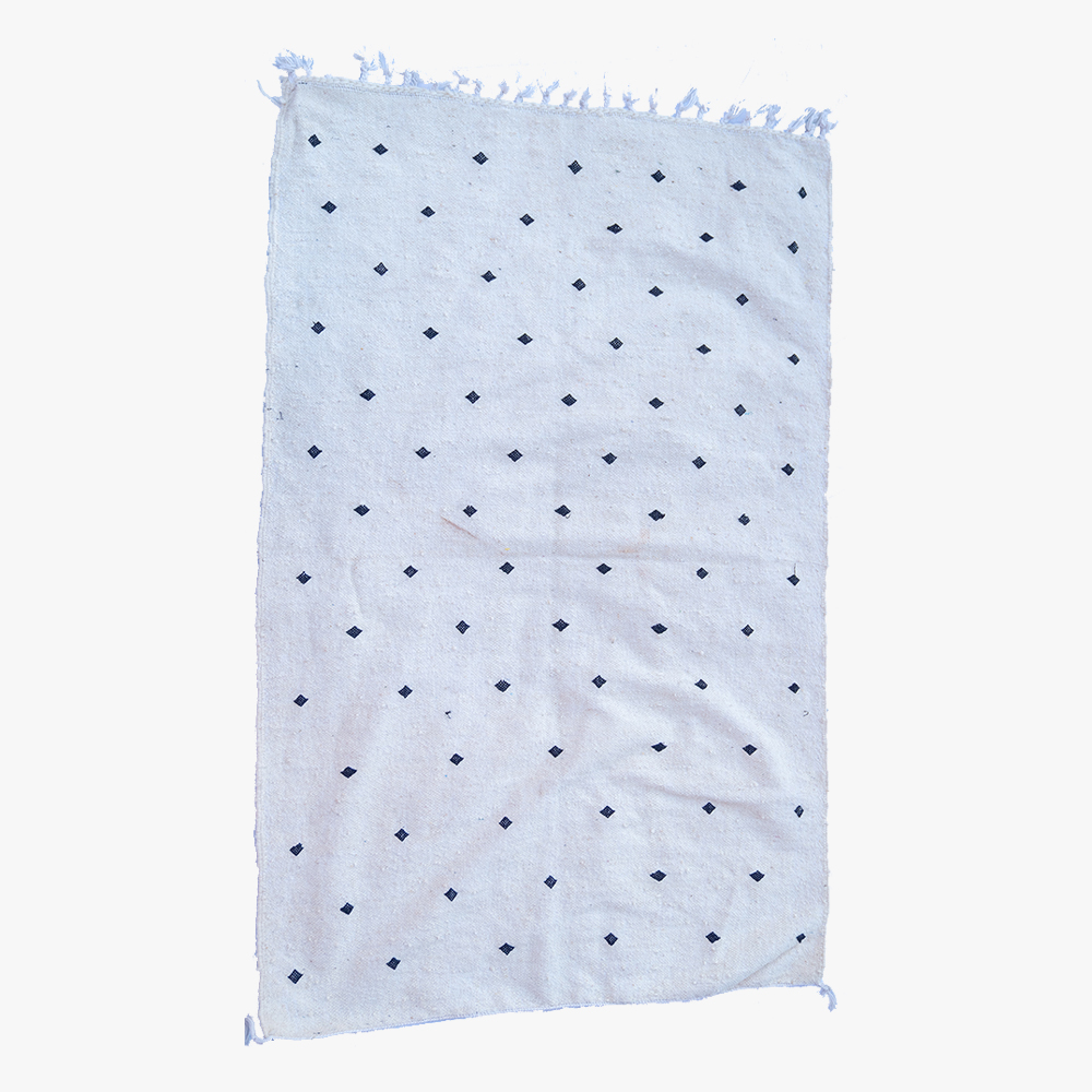 Licht berber tapijt met discrete blauwe stippen en franjes, ideaal voor een elegante en ingetogen huisdecoratie.